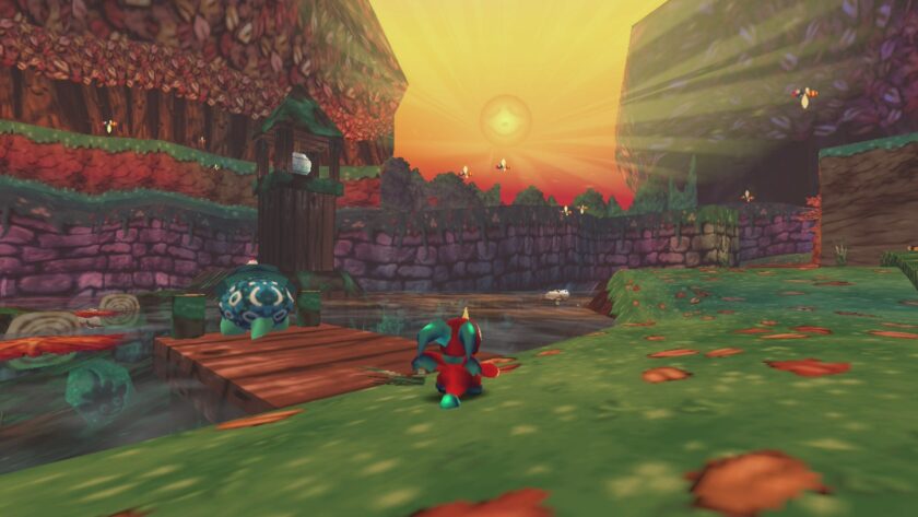 In the video game "Cavern of Dreams", a screenshot captures a fantastical landscape at sunset. A creature with a blue and spotted shell stands on a wooden dock, overlooking a serene river. In the foreground, a bright red and blue character is crouched on vibrant green grass. The scene is bathed in the warm glow of the setting sun, with rays of light piercing through the atmosphere, casting long shadows and a feeling of tranquility. Gentle fires and an orange tree line the stone walls in the distance, enhancing the magical ambiance of this virtual world. Published on: LadiesGamers.