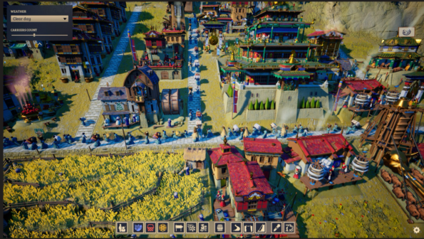 In-game screenshot from Laysara: Summit Kingdom, showcasing a bustling mountain village during a clear day. The village is alive with activity; numerous in-game characters are seen walking through the streets and working in the fields. The scene is detailed with colorful, multi-storied buildings with traditional Eastern architectural influences, golden yellow crop fields, and various decorative elements like flags and banners. A construction site with a large wooden crane indicates ongoing development. The user interface at the bottom of the screen displays a selection of building options and game management tools, with a weather setting and carrier count feature visible in the top left corner. Published on: LadiesGamers.