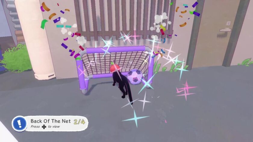 The little kitten wearing a red apple hat, getting the purple ball into the purple goal.
