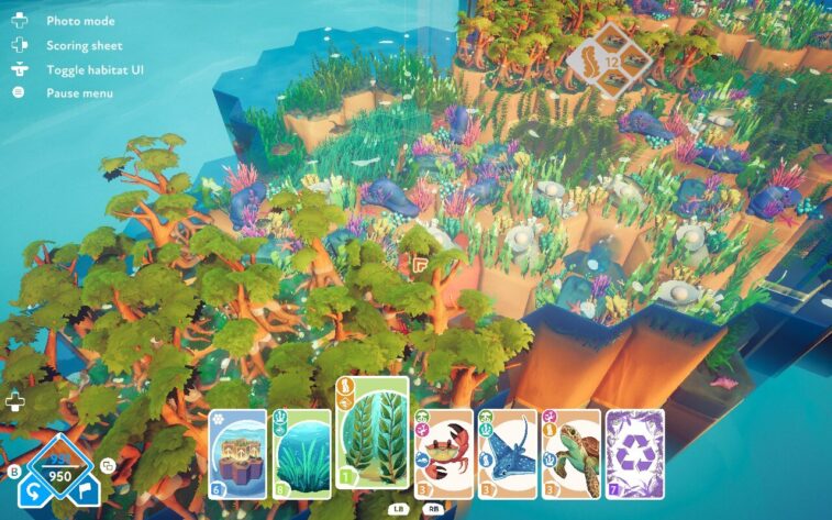 An expansive, vibrant ecosystem on hexagonal tiles with diverse flora and fauna. The bottom of the screen displays various action cards, including plants and marine life. Published on: LadiesGamers.
