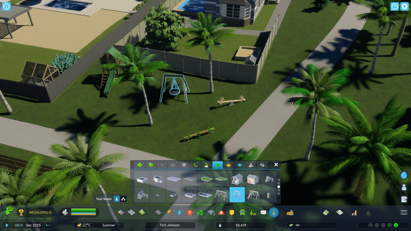 The image shows gameplay from Cities: Skylines II, featuring a suburban area with neatly arranged palm trees, modern houses, and backyard playground equipment like swings and seesaws. The scene is set during summer with clear skies, and the interface at the bottom of the screen displays various building and landscaping options, such as playground equipment and garden items. The game’s HUD indicates that the current time is 08:10 on a day in December 2025, with a temperature of 27°C. The location being developed is named Fort Johnson. Published on: LadiesGamers.