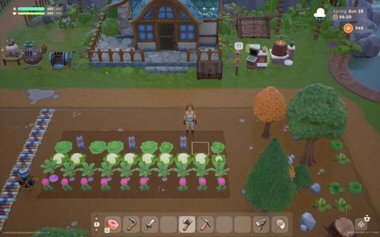 Screenshot of Coral Island shows a player character standing in front of a cozy blue-roofed farmhouse surrounded by lush green grass and a wooden fence. In the foreground, there are neatly arranged vegetable crops, including cabbages, cauliflowers, and turnips, with sprinklers in between. Various tools and crafting stations are visible around the garden, reflecting a well-maintained farm setup.