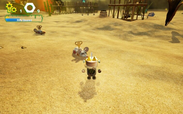 Small robot Buddy in Misc.A Tiny Tale stands in a sandy area littered with wind-up toy mice, while wooden fences and structures loom in the background. The interface shows 39% cleaned progress and 9 bolts collected. Published on: LadiesGamers