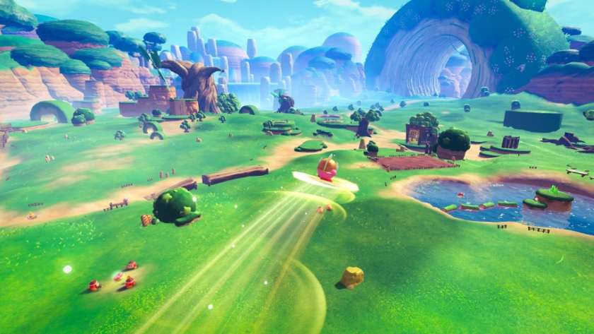 Promotional image from Kirby and the World Beyond showing a vast landscape of trees, a lake and a large rock ring and Kirby gliding through the sky. Published on LadiesGamers